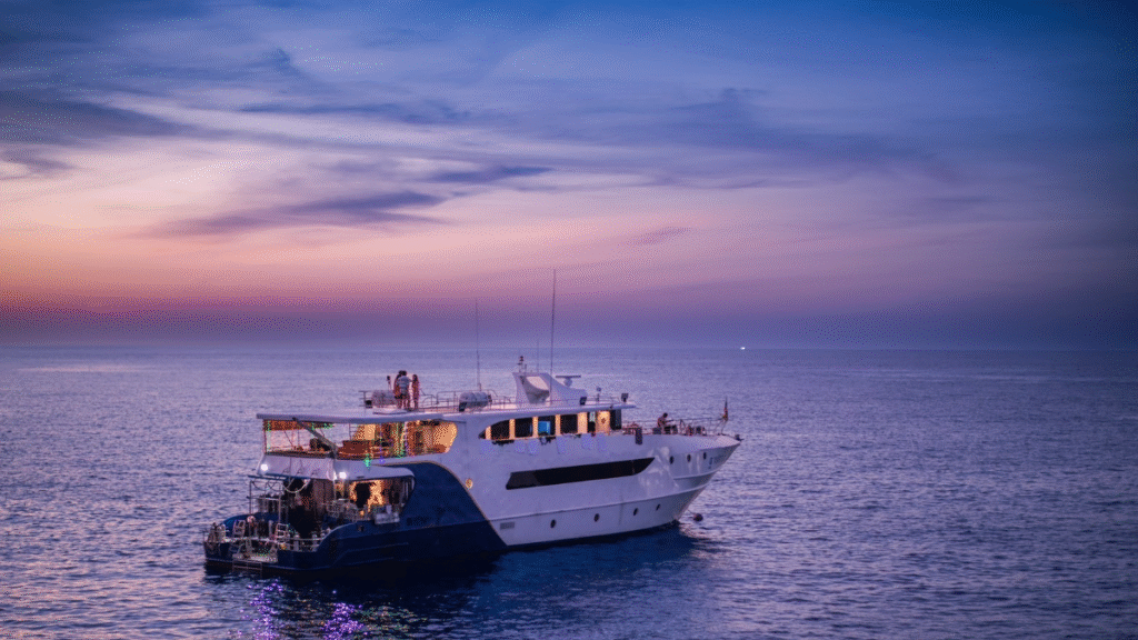 The MV Aqua liveaboard boat cruising in the Andaman Sea, illuminated by a vibrant purple and pink sunset.