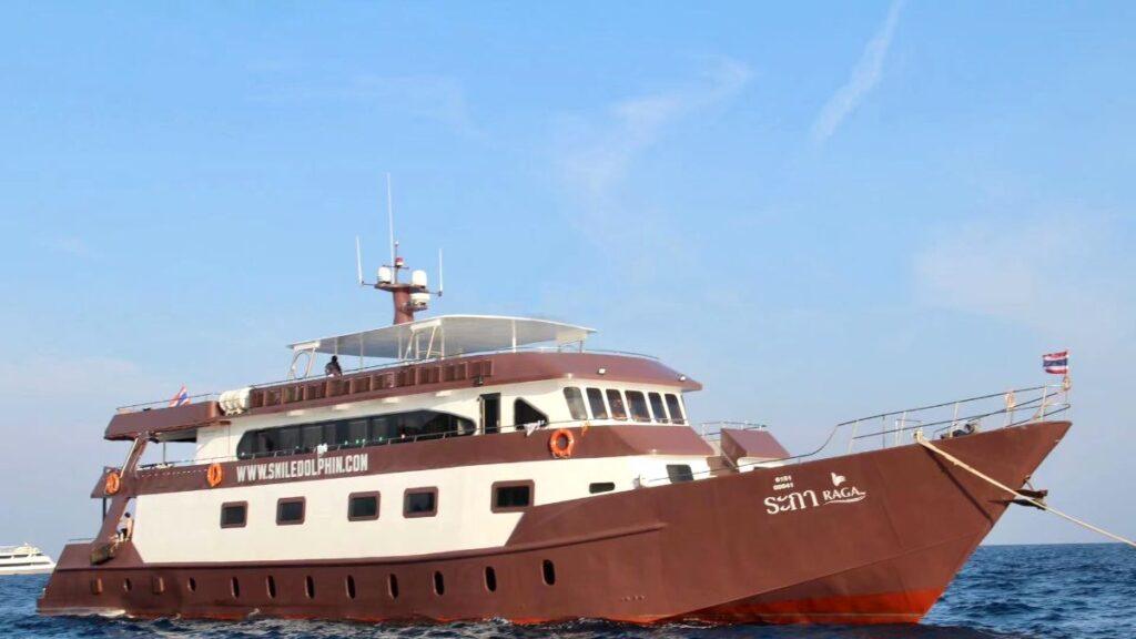 The MV Raga, a brown and white liveaboard dive boat, cruising in the clear blue waters of Thailand.