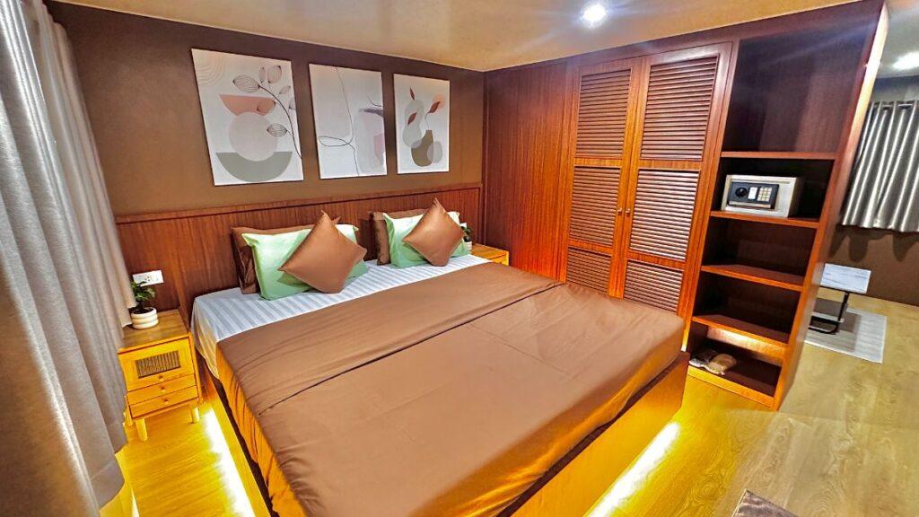 Interior of a spacious master suite cabin on a luxury liveaboard, featuring a large double bed, wood-paneled wardrobe, and a personal safe.
