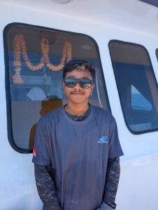 Boy, a deck hand on the MV Raga, smiling coolly with sunglasses on the boat deck.