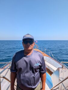 Captain Yord, an experienced boat pilot, standing confidently on the deck wearing sunglasses and a navy cap.
