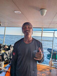 Dinghy driver Nueng giving a shaka sign on the MV Aqua, ready for diver pickup.