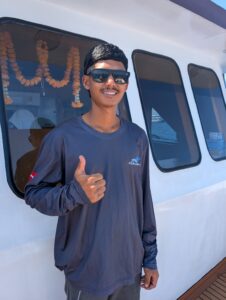 Rit, a deck hand on the MV Raga, giving a confident thumbs up on the boat deck.
