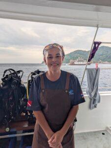 Tip, the chef on MV Gentle Giant, wearing a brown apron and headscarf, smiling on the boat deck.
